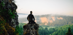Practicing mindfulness - man sitting on a rock in the mountains